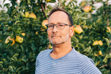 Man farmer posing in apple orchard, wearing stripe t-shirt and glasses