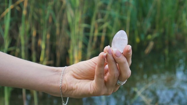 Female hand holding a amethyst crystal yoni egg on river background. Women's health, unity with nature concepts