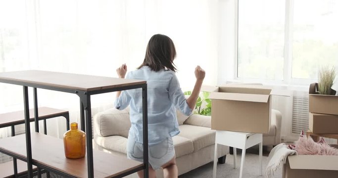 Young woman dancing while unpacking box and decorating her new apartment