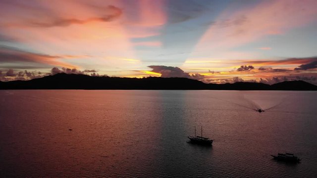 (Long) Aerial video of a scenic orange sunset flying over the water with some boats and clouds.