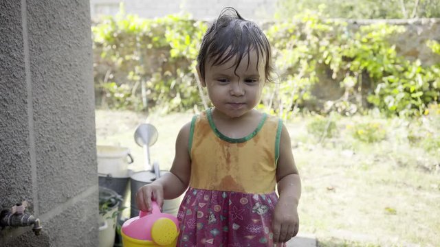 Little girl plays with water on the street, douses herself with water in the yard, joyful and happy