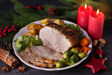 Baked ham with vegetables: potatoes, carrots, brussel sprouts, cabbage and green peas. Christmas decorations. Dish for Christmas Eve