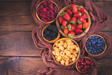 Blackberry, strawberry, yellow and red raspberries, dogwood in wooden bowls on a dark wooden old background in vintage style.