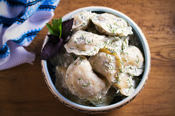 Dumplings filled with potato in sour cream, blue bowl on wooden table - overhead, horizontal