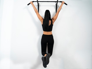 Female hanging on pull ups bar indoors, white wall 