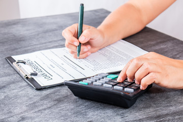 Businesswoman signed a contract loan agreement. Hand signing legal or insurance document or business contract on grey desk. Calculating loan fees. Loan concept.