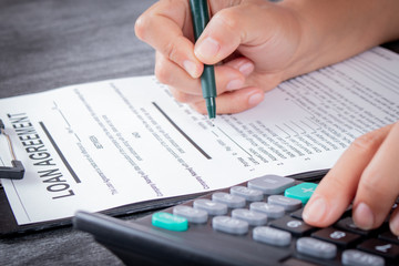 Businesswoman signed a contract loan agreement. Hand signing legal or insurance document or business contract on grey desk. Calculating loan fees. Loan concept.