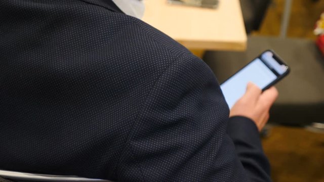 Closeup shot of man in dlack suit holding mobile phone scrolling at business meeting, business conference or presentation, workshop. audience at seminar, texting sms. 4k