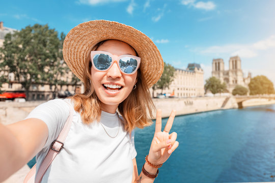 Happy traveler girl blogger takes photos of Notre Dame De Paris and the river Seine for her social media