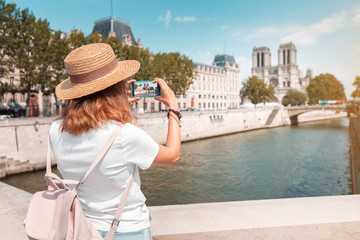 Happy traveler girl blogger takes photos of Notre Dame De Paris and the river Seine for her social...