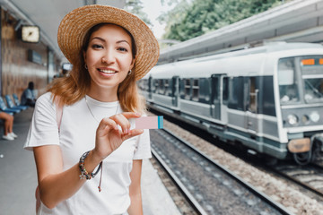 Portrait of an asian girl holding a small electronic smart ticket and waiting for a train on a railroad platfotm. Transportation fee and travel concept