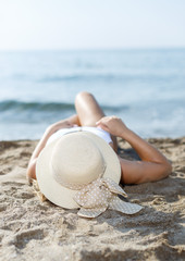 Fototapeta na wymiar Closeup of girl in swimsuit and hat taking sunbath at sandy beach