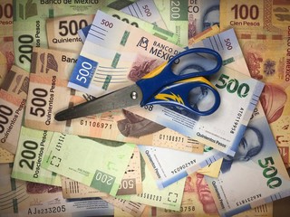 Mexican pesos bills spread randomly over a flat surface with scissors on top