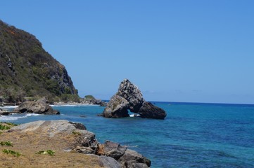 Fototapeta na wymiar playa piedras con formas grandes mar azul con cielo azul paisaje de montaña