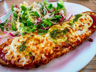 Overhead shot of french break pizza with mixed green salad on white plate