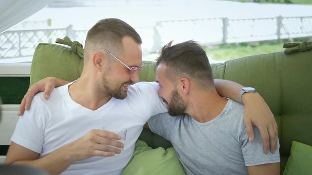 Gay couple smokes a hookah, sitting in the gazebo on the street on a sunny summer day.