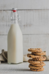 Galletas en primer plano con botella de leche detrás y fondo blanco de madera
