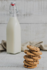 Galletas en primer plano con botella de leche detrás y fondo blanco de madera