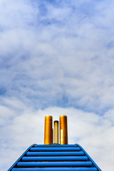 Simple graphic front view of ship exhaust pipes and blue cowling against blue sky with clouds.