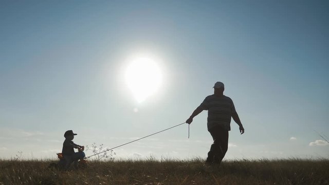 Senior man grandfather teaches his grandson to ride a bike in nature. He pulls it by the rope, the kid learns to ride a bicycle, fun for the family in the outdoor during sunset. Generation concept.