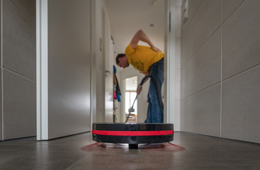 Modern live with a vacuum robot vs a man with a hoover in background with back pain.