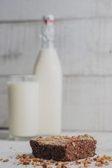 brownie en primer plano con botella y vaso de leche detrás fuera de foco  
