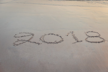 Numbers 2018 handwritten on sand at the beach during sunset time