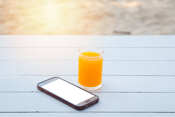 Orange juice in glass and mobile phone on white wooden table