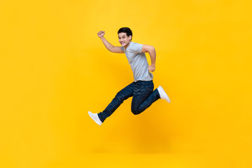 Fototapeta na wymiar Energetic excited young Asian man in casual clothes jumping in yellow background