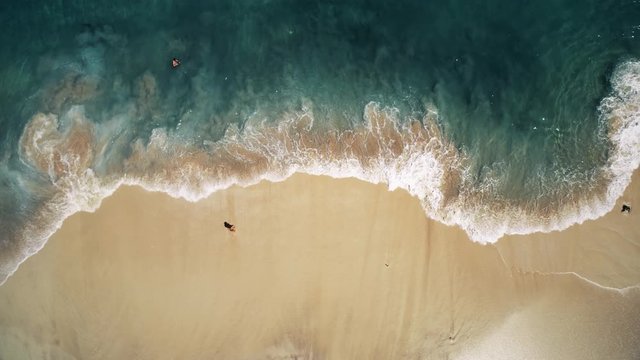 person stands on yellow sand beach at foaming ocean waves rolling on tropical coastline vertical aerial. Concept vacation paradise recreation exotic nature. Nusa Penida Bali island, Indonesia. 4K shot