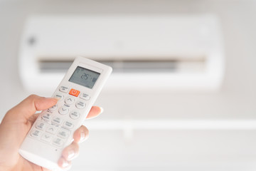 woman hand holding remote controller directed on the air conditioner inside the room and set at ambient temperature,25 degrees celsius.