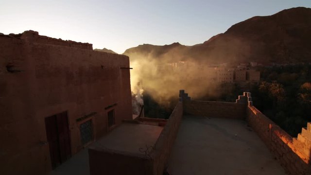 Todra gorge moroccan style kasbah housing in desert with fast moving rooftop smoke rising into sunse