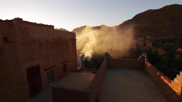 Todra gorge Moroccan style kasbah housing in desert with rooftop smoke rising into sunset