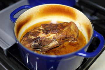 Braised pork roast cooked in a Dutch oven resting on the stove top.