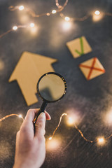 hand holding magnifying glass over miniature cardboard house with green tick and cross options