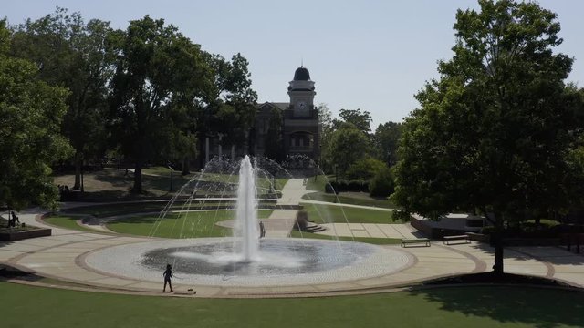 Aerial footage of a young girl silhouetted against a water fountain.
