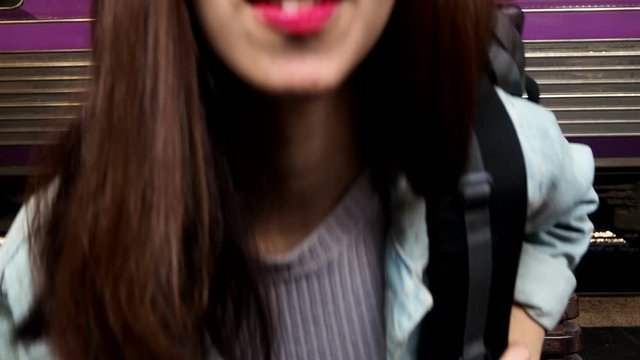 Young Asian smiling traveler woman with backpack blowing air kiss at train station.