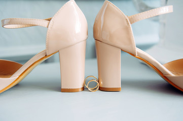 Classic gold wedding rings and beige patent leather bride shoes, close-up. Wedding rings near heels.