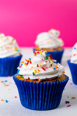 Cupcake saboroso de baunilha com chantily e brigadeiro granulado colorido sobre chuva de esferas azuis mais vela chuva de prata