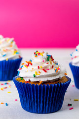 Cupcake saboroso de baunilha com chantily e brigadeiro granulado colorido sobre chuva de esferas azuis mais vela chuva de prata