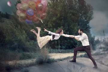 A man holds his hands a girl flying away with balloons. The effect of levitation.