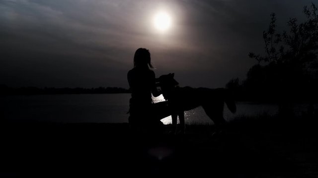 Girl stroking a husky dog at sunset by the river. Glare moon reflected in water