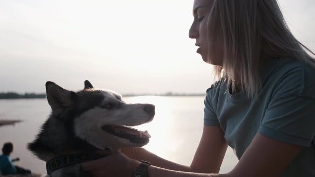 Beautiful young woman and dog Husky Relaxing on Beach Sunset background river
