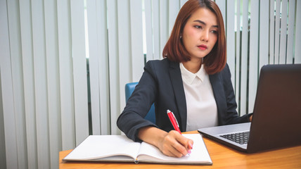Business woman sitting at table and taking notes in laptop