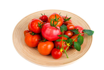 Wooden dish with different ripe tomatoes on white background.
