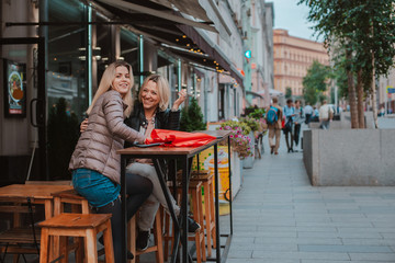 Two young women friends met in a city street cafe and have fun chatting.