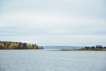 autumn landscape with surface lake water, country house, yellow deciduous and green coniferous forest, and cloudy sky, horizontal stock photo image