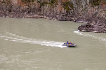 Obraz premium Aerial view of a gray rubber motor boat sailing on a green river in the mountains between rocks and cliff