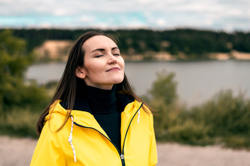 young girl breathes clean fresh cool autumn air in nature near forest lake in yellow raincoat with...