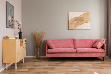 Flowers in vases on wooden commode in contemporary living room interior with pastel pink sofa